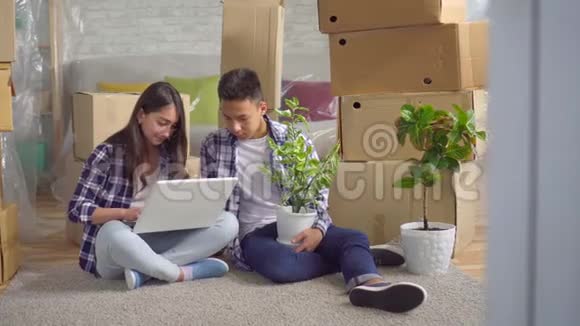 年轻的亚洲夫妇开车进了一间新公寓坐在地上用笔记本电脑视频的预览图
