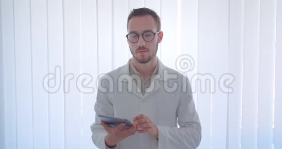 年轻英俊的白种人男医生手持平板电脑在镜头中显示绿色的彩色屏幕视频的预览图