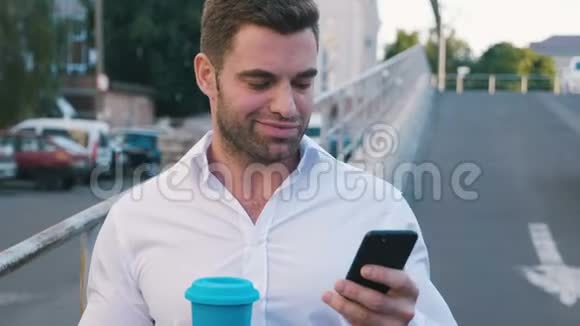 漂亮的商人站在办公楼附近的停车场上在他的智能手机上输入信息美味的饮料视频的预览图