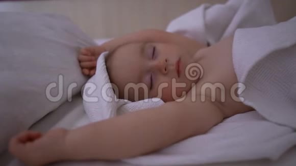 一个光着身子的一岁孩子慢吞吞地睡在白色毯子下面视频的预览图