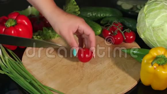 特写女孩在黑色背景的木制砧板上切西红柿视频的预览图