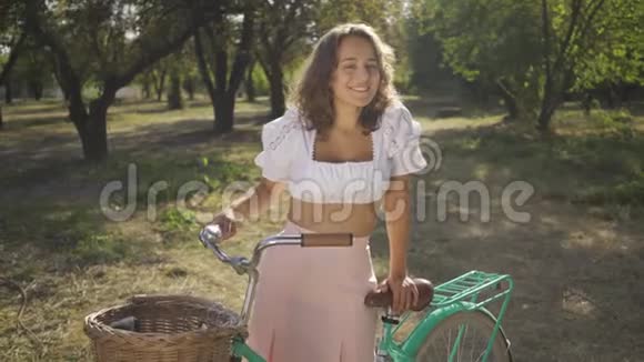 有魅力的年轻女人的肖像卷发骑着自行车站在花园或公园里农村生活复古视频的预览图