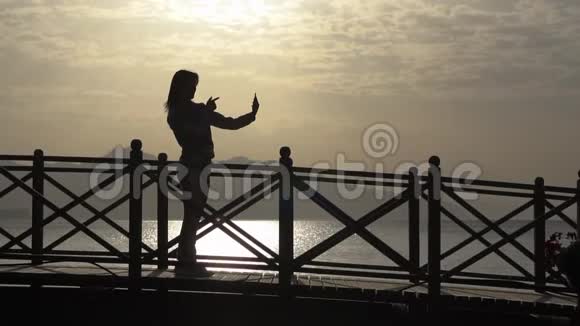 一位年轻女孩用慢动作在海边呼唤智能手机的剪影视频的预览图