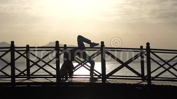 女孩摆出一个桥的姿势在日出时腿靠海抬起动作缓慢视频的预览图
