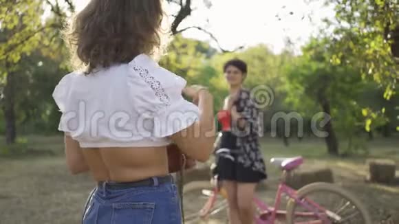 漂亮的白种人年轻女子短发骑着自行车摆姿势而她的朋友在花园里拍照视频的预览图