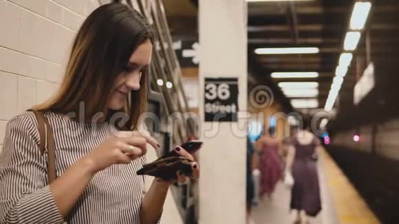 美丽的年轻女子在地铁列车平台上持有智能手机和钱包购买购物在线应用程序视频的预览图