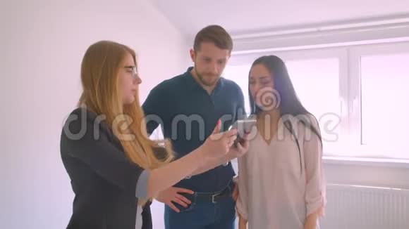 房地产经纪人向年轻的白种人夫妇展示了出售的公寓展示了平板电脑上的机会视频的预览图