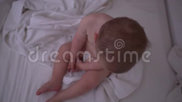一个昏昏欲睡的小男孩坐在床上慢慢地铺着白色的床上用品视频的预览图