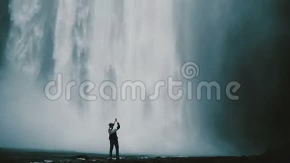 年轻的帅哥在冰岛著名的智能手机上拍照男性走在Gljufrabui瀑布附近视频的预览图