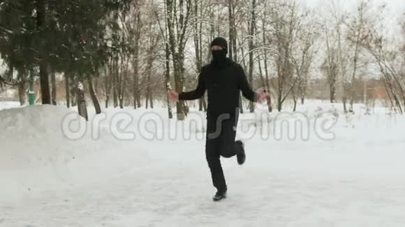 年轻人戴着面具穿着黑色运动服在白雪覆盖的公园里做运动跳绳视频的预览图
