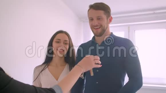 年轻的白种人夫妇从他们的新公寓从房地产经纪人那里得到钥匙接吻是兴奋的视频的预览图