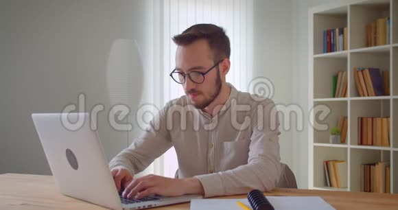 年轻英俊的白种人商人在笔记本电脑上打字看着相机自信地微笑着的特写照片视频的预览图