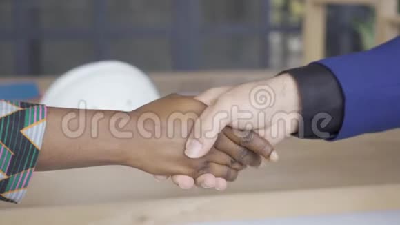 白人男子和非洲裔美国妇女在桌子前握手设计师与客户签订合同视频的预览图