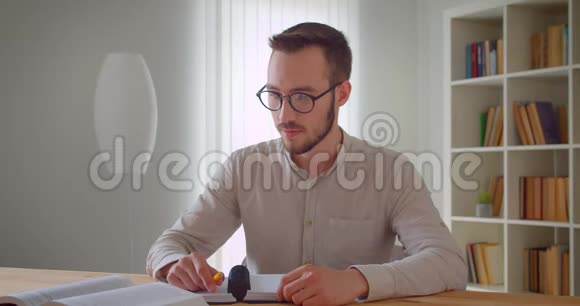 年轻英俊的白种人男性眼镜研究和使用平板电脑笔记的特写照片视频的预览图