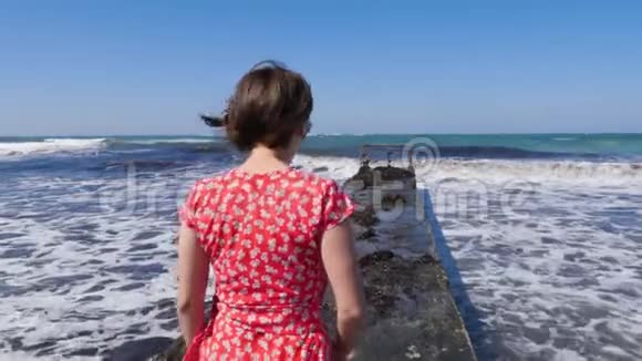 年轻迷人的白种人女人穿着红色的裙子走在码头上赤脚的双腿朝着码头上的大海走去慢节奏视频的预览图
