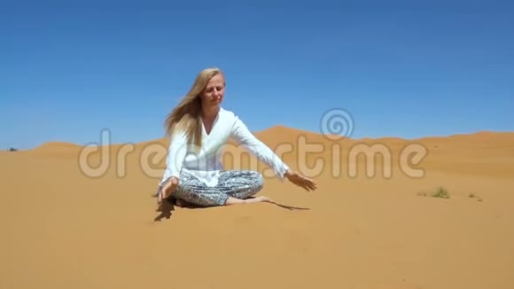沙漠中的金发女人倒沙冥想放松的概念视频的预览图
