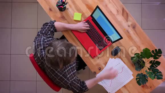一位年轻的高加索商人在桌上的笔记本电脑上打字并在办公室里学习图表的特写镜头视频的预览图