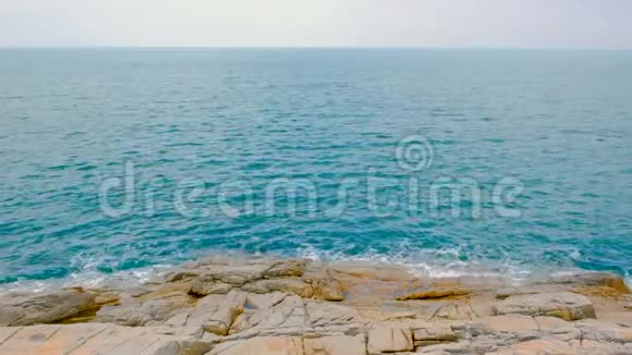 海浪拍打在岩石上泡沫般的海浪来到海岸蓝色的海水和山丘在白天视频的预览图