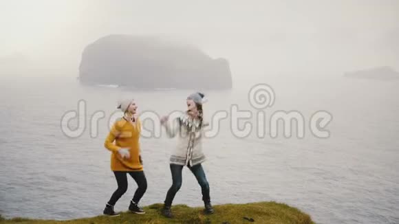 两个快乐的女人在冰岛的海边跳舞愉快的游客探索一个新的国家和乐趣视频的预览图