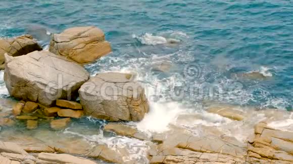 海浪拍打在岩石上泡沫般的海浪来到海岸蓝色的海水和山丘在白天视频的预览图