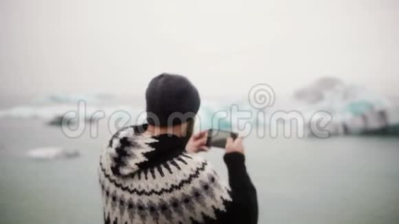 年轻英俊的男人在智能手机上的冰泻湖拍照冰川一个人在冰岛旅行视频的预览图