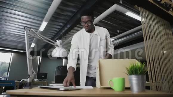 一个非洲男人正搬去新的办公室他正在把个人物品装到纸箱里视频的预览图