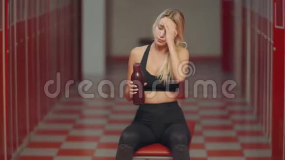 疲惫的女运动员在更衣室里打开运动瓶性感女孩在喝水视频的预览图