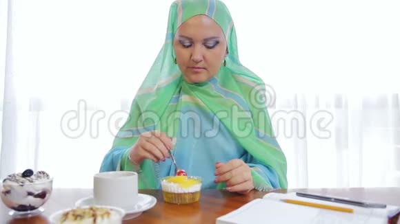 一个穿着浅绿色围巾的年轻穆斯林妇女在咖啡馆里吃蛋糕和喝茶视频的预览图