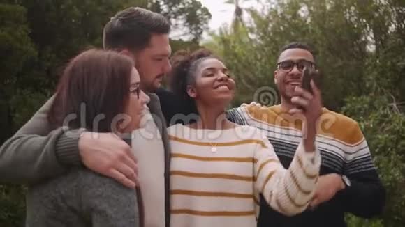 一群快乐的不同朋友站在一起在公园的智能手机上自拍视频的预览图