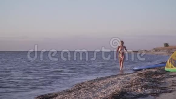 穿比基尼的性感金发女人在日落时沿着海滩奔跑视频的预览图