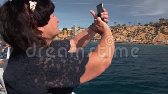 老年女性快乐成年游客在船上使用手机智能手机获得热带岛屿的照片慢动作视频的预览图