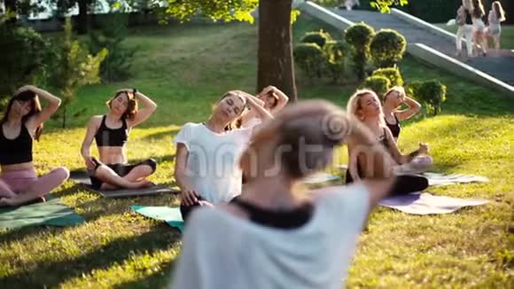 夏季阳光明媚的早晨在教练的指导下一群妇女在公园里倾斜脖子视频的预览图