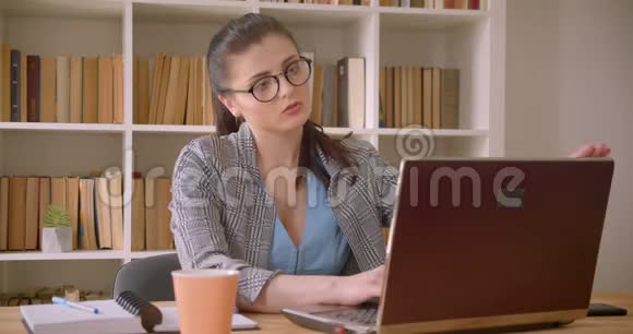 一位年轻成功的高加索女商人戴着眼镜在图书馆办公室室内使用笔记本电脑的特写镜头视频的预览图
