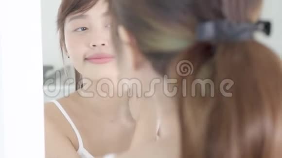美丽的年轻亚洲女人照镜子颈部涂防晒霜美丽的亚洲女孩完美的护肤视频的预览图