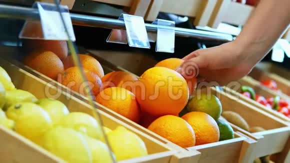 女人手选择五颜六色的橙色在货架上与水果在市场上并采取它的特写视频的预览图