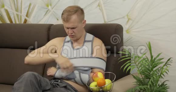 一个痛苦的男人胳膊断了戴着扶手坐在沙发上吃苹果视频的预览图