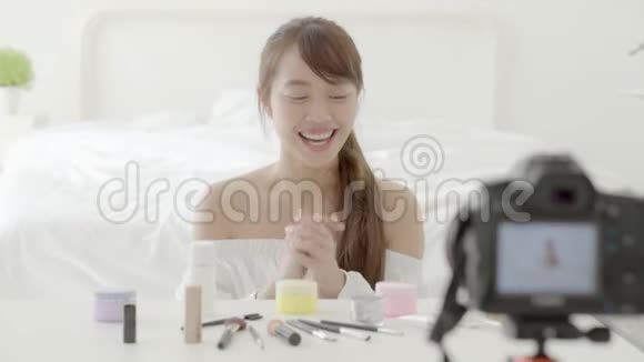 美丽的亚洲年轻女性在家里用视频和vlog显示化妆霜或化妆水视频的预览图