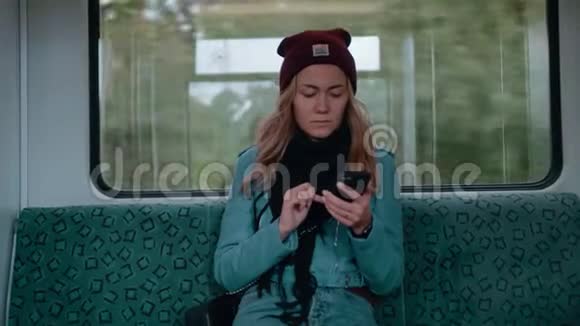 年轻的白种人女孩蓝眼睛坐地铁或电车用电话打印信息看起来视频的预览图