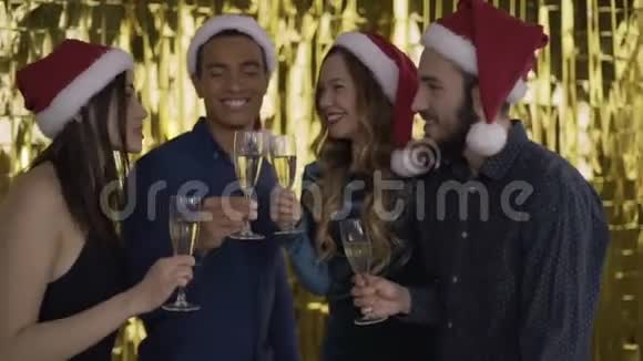 4个人在圣诞晚会上交谈伙计们戴着红帽子的圣诞老人混血儿黄金背景4K视频的预览图