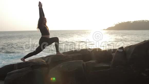 女孩剪影练习瑜伽锻炼站在岩石上视频的预览图