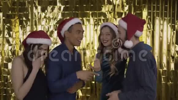 4个人在圣诞晚会上交谈伙计们戴着红帽子的圣诞老人混血儿黄金背景4K视频的预览图
