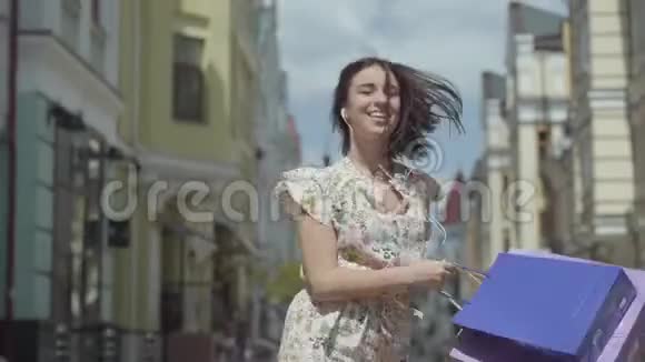 可爱开朗的年轻女人带着购物袋带着耳机和手机的女孩一边听音乐一边跳舞视频的预览图