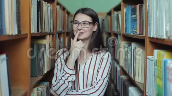 图书馆里年轻漂亮女孩的肖像女学生在书架之间的许多书中学习女孩说话视频的预览图