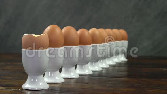 把一个土司士兵端成一个煮熟的鸡蛋放在木桌上的一排白蛋杯里视频的预览图