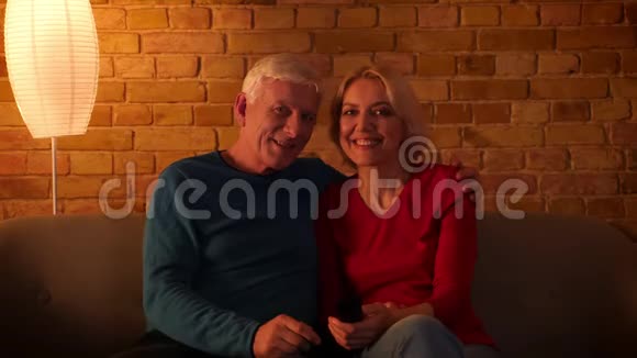 一对高年级幸福夫妇在看电视电影时开心地笑着轻松地坐在室内的沙发上视频的预览图