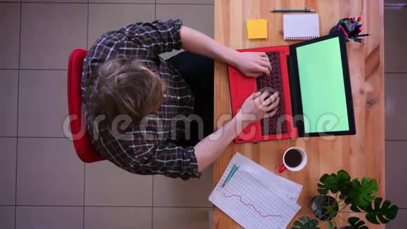 为年轻的高加索商人拍摄的特写镜头他在笔记本电脑上工作用绿色屏幕记录笔记喝酒视频的预览图