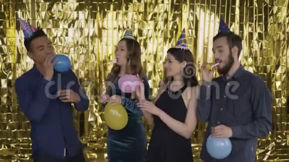 4个混血儿在派对上玩得很开心他们在豪华的金色背景下充气气球吹吹烟斗视频的预览图