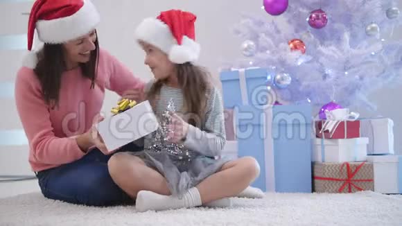 在新年的时候在圣诞树附近的地毯上一位细心的妈妈送礼物给她的女儿视频的预览图