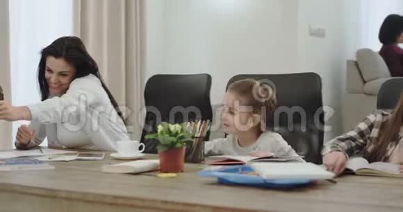 忙碌的成熟的母亲和她的三个孩子在客厅里做作业时在电话里交谈视频的预览图