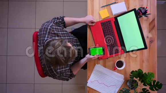 年轻的高加索商人用绿色屏幕在笔记本电脑前滚动手机的特写镜头视频的预览图
